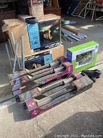 Four Geisha Mark'r Lite yard lights in original boxes with transparent covers showing tube lights, laid on pavement next to boxes containing outdoor lighting and yard decorations.