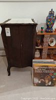 Front view of antique wooden record stand cabinet with two closed doors and label tag visible.