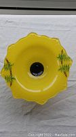 Top view showing scalloped edges and green leaf motifs inside the yellow glass bowl.