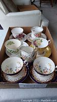 Overview of six teacups and six saucers with creamer and sugar dish in cardboard tray