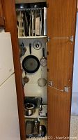 Same open cabinet showing hanging pans, strainers, and a stainless steel pot on bottom shelf.