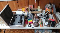 Wide view of table with multiple vintage cameras, accessories, slides, film canisters, and carrying case displayed