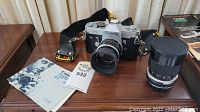 Canon FT 35mm film camera with Canon FL 50mm f/1.8 lens, Tamron zoom lens, camera strap, and manuals on a wooden table