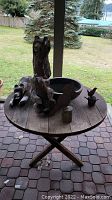 Round wooden table with metal rim viewed outside on patio with two wooden bear sculptures and other small items on top.