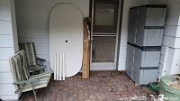 Two metal folding chairs with striped cushions, folded oval patio table with metal legs, patio umbrella leaning on a porch wall