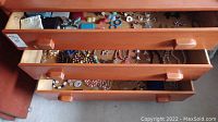 Three wooden drawers shown open revealing various pieces of costume jewelry: necklaces, earrings, bracelets, hat pins and small boxes.