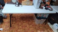 Full side view of the 6ft folding table showing the tabletop, black metal legs, and various objects on table (not included).