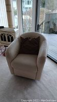 Front view of the cream leather swivel chair with a brown pillow placed on it, showing the upholstery and shape.