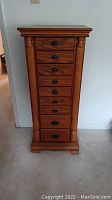 Full view of tall wood jewelry stand showing front with seven drawers and carved side pillars.