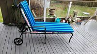 Metal lounge chair with blue striped cushion shown on porch, displaying wheels and adjustable backrest.