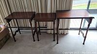 Three mahogany Baetz nesting tables arranged side by side, showing front and side views, in need of refinishing with visible wear.