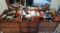 Photo showing multiple men's wallets, handkerchiefs, socks, and other men's accessories arranged on a wooden dresser surface.