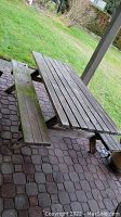 Overall view of wooden picnic table with attached benches on brick patio and lawn background