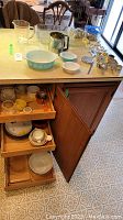Three wooden drawers with various baking dishes including Pyrex and other vintage kitchen items; top drawer also contains measuring cups and sifter on counter