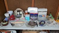 Full view of table with various kitchen items including the Sunbeam mixer, Pyrex bowls, meat grinder, casserole dish, rolling pin and multiple small kitchenware pieces