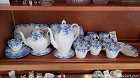 Full view of set on shelf showing coffee cups, platters, bread plates, teapot and coffee pot
