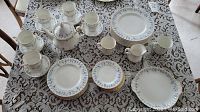 Overhead view of table with dinnerware items, including plates, cups, saucers, teapot and creamer on lace tablecloth