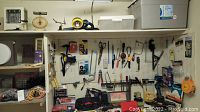 Photo showing pegboard with various hanging hand tools like scissors, pliers, wrenches, and clamps alongside a metal vice and BluePlanet storage tote beneath.