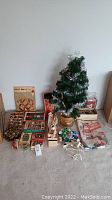 Wide photo showing entire lot: artificial Christmas tree with silver tinsel, multiple boxes of ornaments and other decorations arranged on floor.