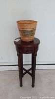 Full view of the round dark wood pedestal table with the woven basket placed on top, showing table design and basket.