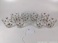 Front view of all 8 clear glass tumblers displaying black and gold mid-century patterns, arranged in two rows.