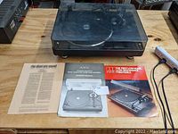 Turntable with clear dust cover on wooden table with documentation underneath