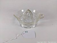 Front view of clear glass citrus juice reamer with criss cross pattern, handle and pouring spout.