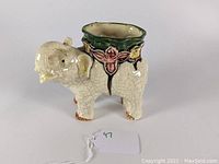 Side view showing elephant shape, crackled cream glaze, floral design, and green rim opening.