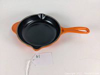Top view of orange enameled skillet showing whole cooking surface and handle with number tag