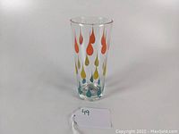 Side view of a tall clear glass highball tumbler with orange, yellow, and teal raindrop decorations.