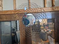 Full view of the round mirror mounted on a wooden wall with visible surrounding workspace reflecting in the mirror.