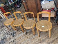 Four chairs arranged in a row on workshop floor showing frames and cane seats.