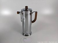 Front angled view of the tall chrome cocktail shaker with walnut handle and knob on a white background.