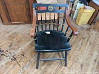 Front angle photo of the vintage Harvard chair showing wooden armrests, black painted seat, and legs on wood flooring.