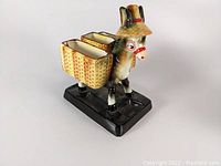 Front and left side angle view of vintage pottery donkey figure with baskets on black base.