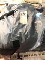 Blue carrying bag with black carry strap containing the air bed, tagged with auction lot sticker.