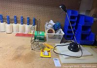 Wide view of lot contents showing stretch wrap rolls, tape basket, paper towel holder, desk lamp, and some cutting boards on a pegboard shelf