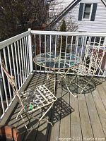 Photo showing wrought iron round table and two foldable wrought iron chairs on wooden deck balcony.