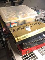 Stack of board games with Backgammon, Scattergories, and Monopoly on metal shelf with plastic bin of books on top.