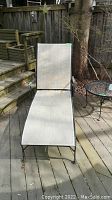 Adjustable chaise lounger made of wrought iron with mesh seating, shown standing on an outdoor deck.