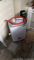 Frigidaire dehumidifier with stand fan in background, red hose and manual on top of dehumidifier
