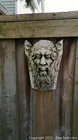 Bearded male face wall sculpture attached to wooden fence, showing detail and texture
