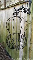 Close-up image of one wrought iron hanging planter cage attached to an outdoor decorative mount on a wooden fence.