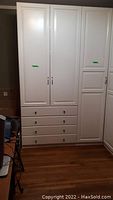 Front view of three white IKEA PAX wardrobe modules showing left double-door unit with three drawers and right narrow solid door unit