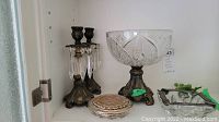 Wide view showing two brass candleholders with hanging crystals, crystal fruit bowl on brass pedestal, small round mosaic coasters, and silvertone ashtray on shelf