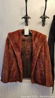 Front view of brown mink fur coat hanging showing full coat and inside brown lining.