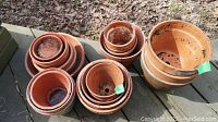 Multiple stacks of clay planters arranged outdoors, showing different sizes nested inside each other with some soil residue inside.