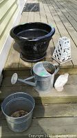 Photo showing all items on wooden steps: black metal planter, galvanized watering can, large pot, white bird figurine, and white floral decor.