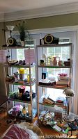 Photo showing two matching gray plastic utility shelves filled with various household items in corner near windows.