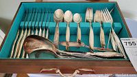 Full set of silverplate cutlery in wooden storage tray, includes knives, spoons, forks, and serving utensils.